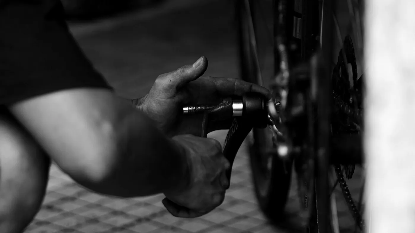 A mechanic's hands driving a tool into a bicycle's rear hub, the cassette and chain alongside. Black and white.