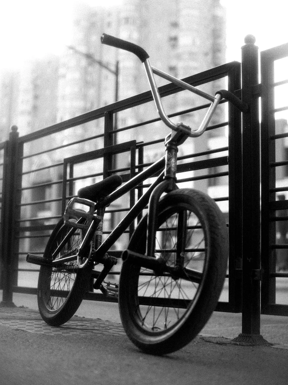 A BMX-style city bike leaning on a steel railing with an apartment block behind, black and white.