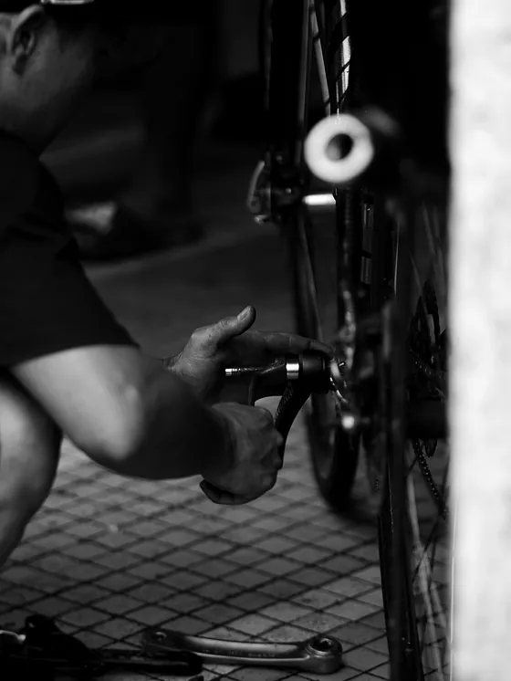 A mechanic working on a bicycle's rear hub with a tool, black and white.