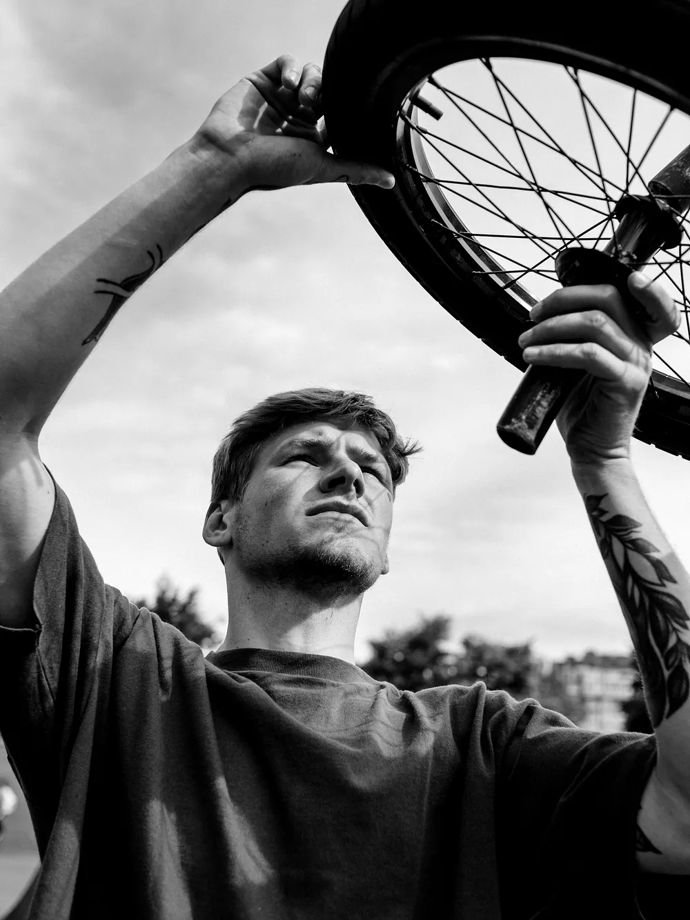 A rider holding a wheel above their head against the sky, black and white.